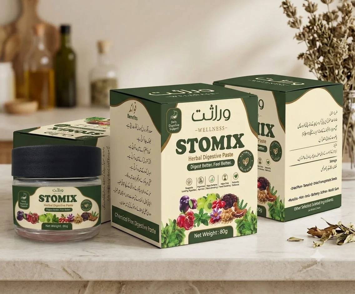Stomix herbal digestive paste packaging displayed on a marble countertop, including a small jar with a black lid, two tall product boxes, and blurred bottles and dried flowers in the background.
